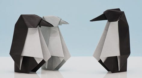 three origami penguins are standing next to each other on a table .