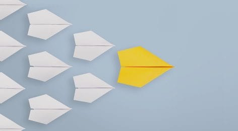 a yellow paper airplane is leading a group of white paper airplanes .